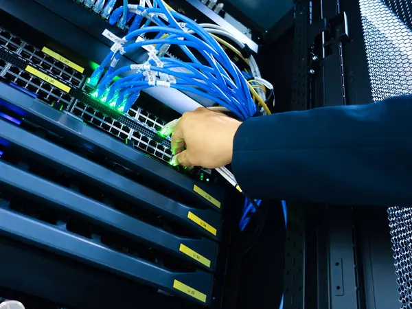 Bir teknisyenin eli, modern altyapılarda veri yönetimi ve iletişim için gerekli teknolojiyi vurgulayarak, sunucu rafındaki ağ kablolarını ayarlar.