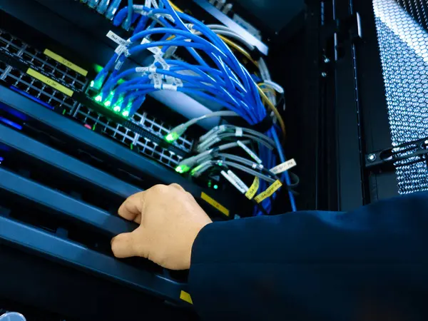 Bir teknisyen bir veri merkezinde sunucu bakımı yapar. Kabloları ve bağlantıları gösterir. Görüntü, çok önemli teknoloji çalışmaları ve organizasyonları vurguluyor.