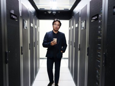 Profesyonel bir adam, gösterişli sunucularla çevrili bir veri merkezinde güvenle durur. Bu görüntü modern teknoloji ve iş çözümlerinin özünü yakalar..