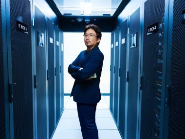 Kendine güvenen bir profesyonel, günümüz dijital ortamındaki teknoloji ve yeniliğin özünü somutlaştıran sunucu raflarıyla çevrili modern bir veri merkezinde duruyor..