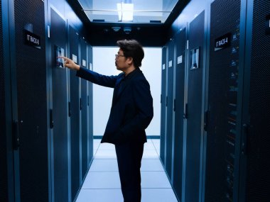 Odaklanmış bir bilişim teknisyeni modern bir veri merkezinde yüksek teknolojili sunucu raflarıyla etkileşime geçerek ağ yönetimi ve sistem bakımı alanında uzmanlık gösteriyor..