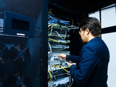 Bir teknisyen bir sunucu rafı içinde çalışır, ağ kablosu ve ekipmanlarını yönetir. Sahne, modern teknoloji ve bilişim operasyonlarının özünü yakalıyor..