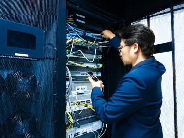 Yetenekli bir teknisyen bir ağ sunucu rafının bakımını üstlenir, kabloları yönetir ve modern teknoloji ortamında verimli bir çalışma sağlar.