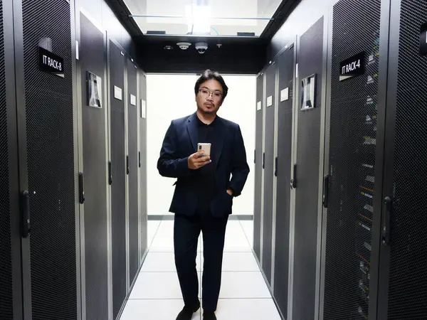 Profesyonel bir adam, gösterişli sunucularla çevrili bir veri merkezinde güvenle durur. Bu görüntü modern teknoloji ve iş çözümlerinin özünü yakalar..