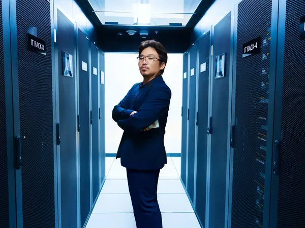 Kendine güvenen bir profesyonel, günümüz dijital ortamındaki teknoloji ve yeniliğin özünü somutlaştıran sunucu raflarıyla çevrili modern bir veri merkezinde duruyor..