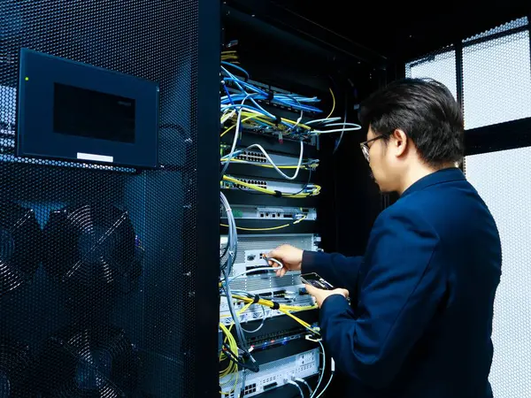 Bir teknisyen bir sunucu rafı içinde çalışır, ağ kablosu ve ekipmanlarını yönetir. Sahne, modern teknoloji ve bilişim operasyonlarının özünü yakalıyor..