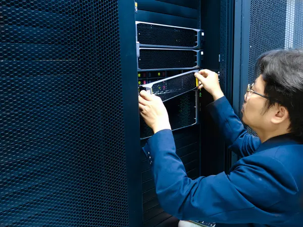 Bir teknisyen veri merkezindeki bir sunucu rafındaki bileşenleri ayarlar. Görüntü, teknoloji yönetiminin özünü, bakımı ve güvenli veri operasyonlarının önemini yakalar..