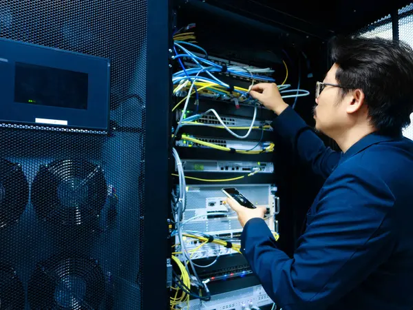 Bir teknisyen modern bir sunucu odasında ağ ekipmanlarını yapılandırıyor. Görüntü, IT bakımını vurgulayarak, kablo ve teknolojiyi düzenledi.