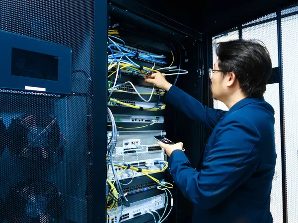 Bir teknisyen, kablolar ve teknolojiyle dolu modern bir ortamı sergileyerek veri merkezinde ağ ekipmanlarını ayarlıyor ve bilişim bakım ve desteğini vurguluyor..