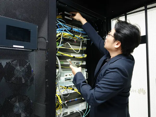 Bir teknisyen modern bir veri merkezinde kablo ve donanım organizasyonunu sağlamak için sunucu rafı içindeki ekipmanları dikkatle yönetir..