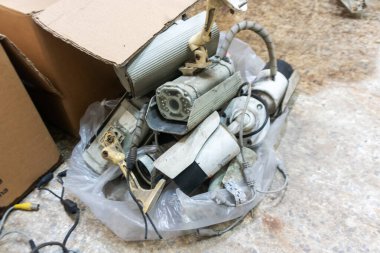 Çöpe atılmış elektronik parçalar ve geri dönüşüme hazır karton bir kutuda toplanmış cihazlar. Çeşitli materyaller e-atık yönetim konularında ipucu veriyor.