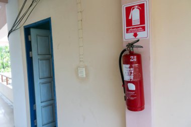 Duvara monte edilmiş canlı kırmızı bir yangın söndürücü, kapalı ortamlardaki temel güvenliği sembolize ediyor. Yangını önleme ve acil durum hazırlığı için ideal.