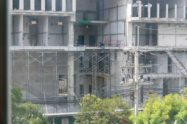 Bir inşaat işçisi, inşaat geliştirme çalışmalarının içerdiği emek ve güvenlik önlemlerini gözler önüne sererek, yoğun bir alandaki iskeleler üzerinde dikkatle çalışır..