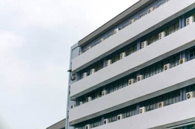 Modern bir binanın dış görüntüsü birden fazla klima ünitesi sergiliyor. Mimari tasarım bulutlu bir gökyüzüne karşı temiz çizgiler içerir..