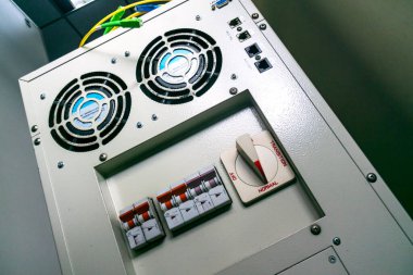 Çalışma ortamlarında teknolojiyi temsil eden şalterler, göstergeler ve soğutma vantilatörlerinin yer aldığı endüstriyel kontrol panelinin yakın görüntüsü.