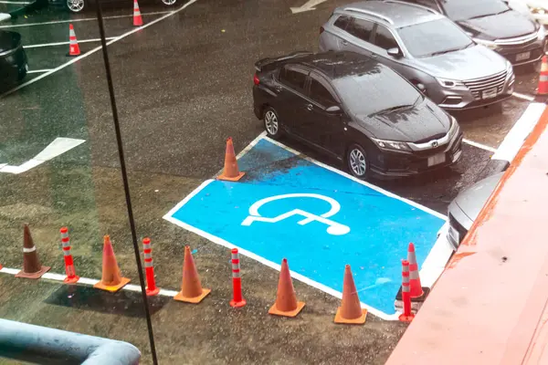 Bu görüntü, yağmurlu havalarda güvenlik konileri ile çevrili mavi ile işaretlenmiş ulaşılabilir bir park alanını gösteriyor. Sahne kentsel altyapı ve erişilebilirlik bilincini vurguluyor.