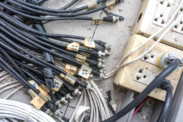 Zemine saçılmış karmaşık kablolar ve güç şeritlerinin yakın çekim görüntüsü. Bu resim elektronik ayarlarda kabloların karmaşıklığını, organizasyon zorluklarını betimler.