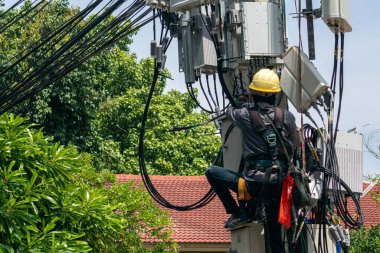 Bir teknisyen güvenli bir şekilde elektrik direğine tırmanıp şehir ortamında iletişim kablolarının ve altyapının bakımını yapar..