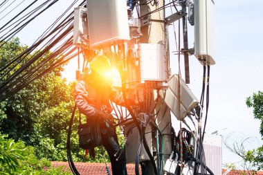 Bir teknisyen, kablolar ve ekipmanlarla çevrili bir elektrik direği üzerinde bakım çalışması yaparak, kentsel altyapının kritik rolünü gözler önüne seriyor..