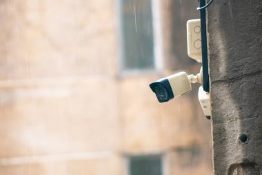 Binaya monte edilmiş bir güvenlik kamerası görüntüsü. Yağmur arka planda yavaşça yağar ve kasvetli bir şehir atmosferi yaratır..