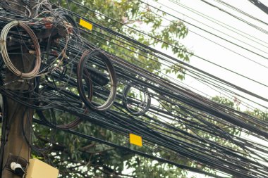 Elektrik kablolarından oluşan karmaşık bir ağ ve elektrik kablolarının elektrik direğindeki yakın plan görüntüsü, kentsel altyapının karmaşık dizaynını ve kaosunu vurguluyor..