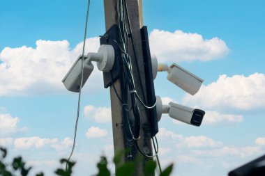 Parlak mavi bir gökyüzünün altında bir telefon direğine monte edilmiş üç güvenlik kamerası. Görüntü, kentsel güvenlikteki izleme teknolojisinin önemini vurguluyor.