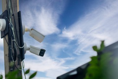 İnce bulutlarla dolu çarpıcı mavi gökyüzüne karşı bir direğe monte edilmiş güvenlik kameraları kentsel alanlarda ihtiyatı ve güvenliği sembolize ediyor..