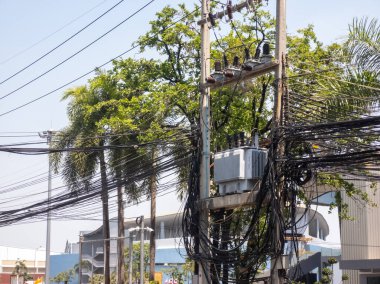 Elektrik hatlarının detaylı bir görüntüsü ve yeşil ağaçlarla çevrili bir trafoda doğa ve altyapının karışımını gözler önüne seriyor..
