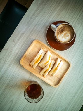 Lezzetli bir sandviç tabağının yanında rahat bir şekilde uzanmak, rahatlatıcı bir kahvaltı için mükemmel ya da günlük bir kafe ortamında öğleden sonra atıştırması için..