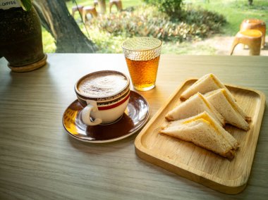 Bir fincan kahve, bir bardak çay ve güneşli bir açık hava ortamı ile çevrili ahşap bir masada bir tabak sandviçin yer aldığı hoş bir sahne. Anın tadını çıkar.!