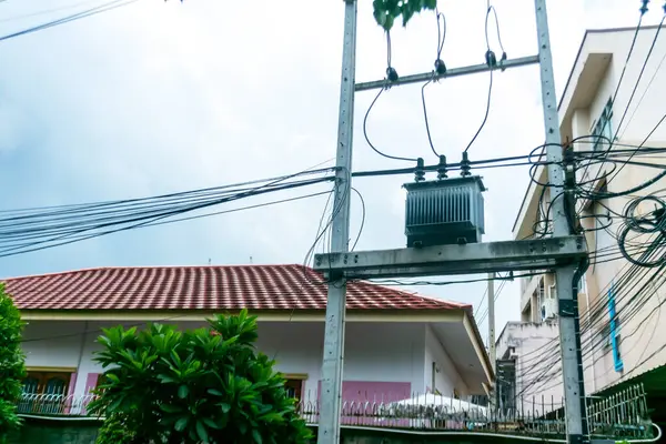 Şehir merkezindeki kablolar, trafo ve bulutlu bir gökyüzünün altında bir yerleşim yeri olan elektrik dağıtım şebekesinin görüntüsü..
