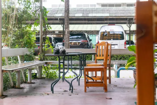 Bereketli yeşilliklerle çevrili ahşap bir sandalye ve masa içeren rahat bir açık kafe oturma alanı, kentsel bir ortamda dinlenmek için sakin bir alan yaratıyor..