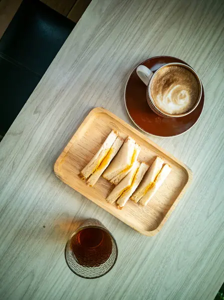 Lezzetli bir sandviç tabağının yanında rahat bir şekilde uzanmak, rahatlatıcı bir kahvaltı için mükemmel ya da günlük bir kafe ortamında öğleden sonra atıştırması için..