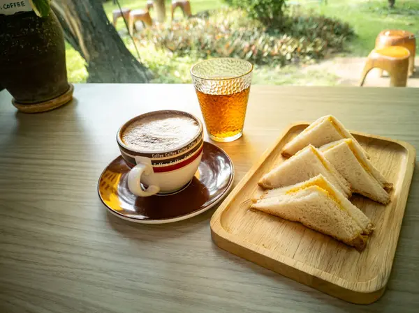 Bir fincan kahve, bir bardak çay ve güneşli bir açık hava ortamı ile çevrili ahşap bir masada bir tabak sandviçin yer aldığı hoş bir sahne. Anın tadını çıkar.!