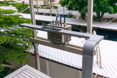 Bir binanın çatısına monte edilmiş bir endüstriyel güç transformatörünün yakın plan görüntüsü, modern ortamdaki elektrik donanımı ve kentsel mimari unsurları sergiliyor..