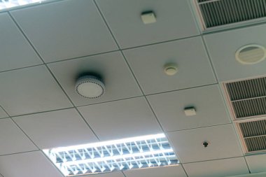 Tepe ışıkları ve sensörlerle donatılmış modern ofis tavanı tasarımı. Temiz çizgiler ve minimalist estetik çalışma ortamı ve işlevselliği artırır.