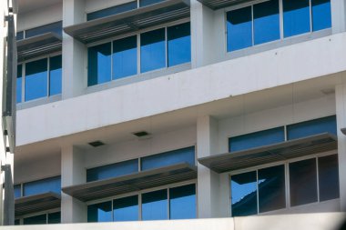 Yansıtıcı camla modern ofis pencerelerinin yakın plan görüntüsü. Temiz çizgiler ve geometrik şekiller çağdaş bir mimari estetik yaratıyor..