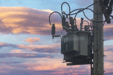 Elektrik direğine monte edilmiş, elektrik bağlantılarının ve altyapının karmaşık detaylarını gösteren yakın plan bir transformatör görüntüsü..