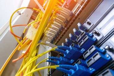 Bir veri merkezi rafındaki fiber optik kabloların ve konnektörlerin yakın plan görüntüsü yüksek hızlı iletişim için gerekli karmaşık kablolar ve ağ altyapısını gösterir.