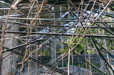 İnşaat alanındaki iskelenin detaylı bir görüntüsü, karmaşık çizgiler ve malzemelerin sergilenmesi, kentsel bir çevredeki inşaat sürecinin vurgulanması.