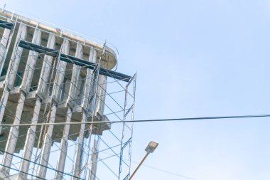Açık mavi gökyüzüne karşı bina yapısını destekleyen inşaat iskelesinin detaylı bir görüntüsü. Sahne, kentsel gelişimin özünü yakalıyor..