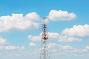 Çarpıcı bir kırmızı-beyaz radyo iletim kulesi bulutlu bir gökyüzünü noktalıyor, modern iletişim teknolojisini ve insanları birbirine bağlamadaki hayati rolünü simgeliyor..