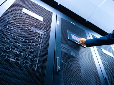 Profesyonel bir el modern bir veri merkezinde teknoloji ve ağ yönetimini gösteren bir sunucu rafındaki kontrol paneline uzanır..