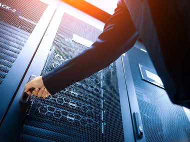 Modern bir veri merkezinde veri yönetimi ve altyapı kontrolünde teknolojinin önemini vurgulayan bir işletme profesyoneli sunucu kabinesine uzanır.