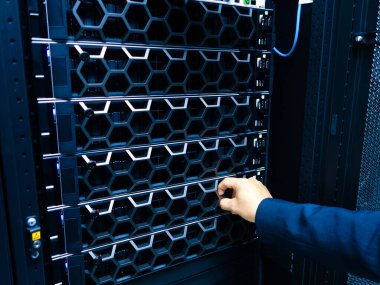 Profesyonel bir el veri merkezindeki bir sunucuya uzanıyor, teknolojinin karmaşıklığını ve modern bilişim ortamlarında ekipman yönetiminin önemini vurguluyor..