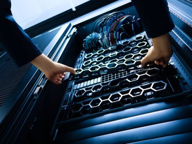 Modern bir veri merkezinde sunucu rafında bakım yapan bir teknisyen. Toplantının odak noktası donanım yükleme ve kabloları yönetme.