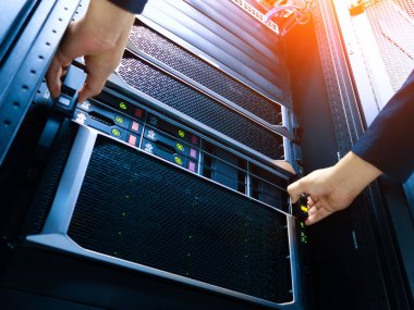 Bir teknisyen veri merkezi rafına bir sunucu yerleştiriyor, modern bilgisayar ortamları için gerekli karmaşık teknoloji ve donanımı sergiliyor.