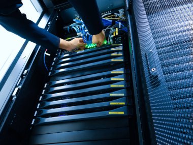 A technician works meticulously inside a server rack, connecting cables and ensuring optimal operation of network hardware in a modern data center environment.