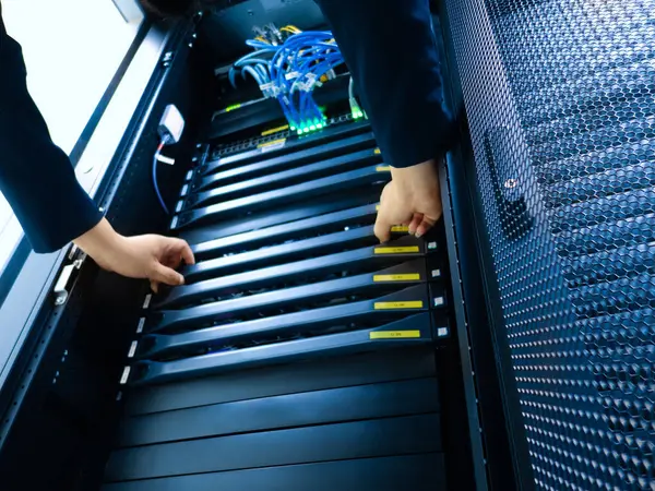 Sunucu rafındaki ellerin ekipmanlarla nasıl başa çıktığına yakın çekim görüntüsü. Bu ayar, etkili veri yönetimi ve bağlantı için hayati önem taşıyan karmaşık kablo ve organizasyonu vurgular.