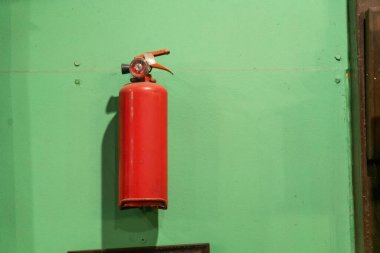 Yeşil bir duvara monte edilmiş parlak kırmızı bir yangın söndürücü endüstriyel ve ticari alanlardaki güvenlik ve acil durum hazırlığını simgeliyor..